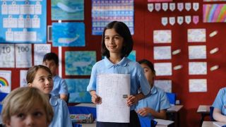 Girl standing in front of class showing artwork